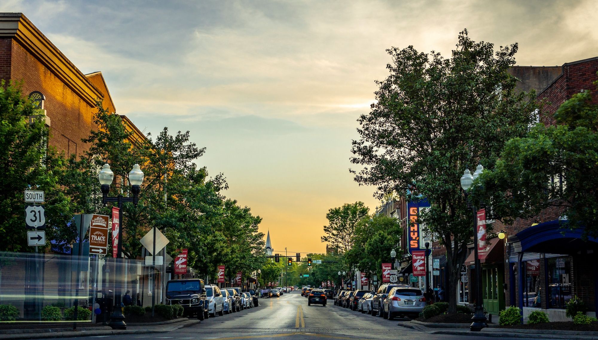 View of downtown Franklin with sunset in the background, trees, and cars on each side.
